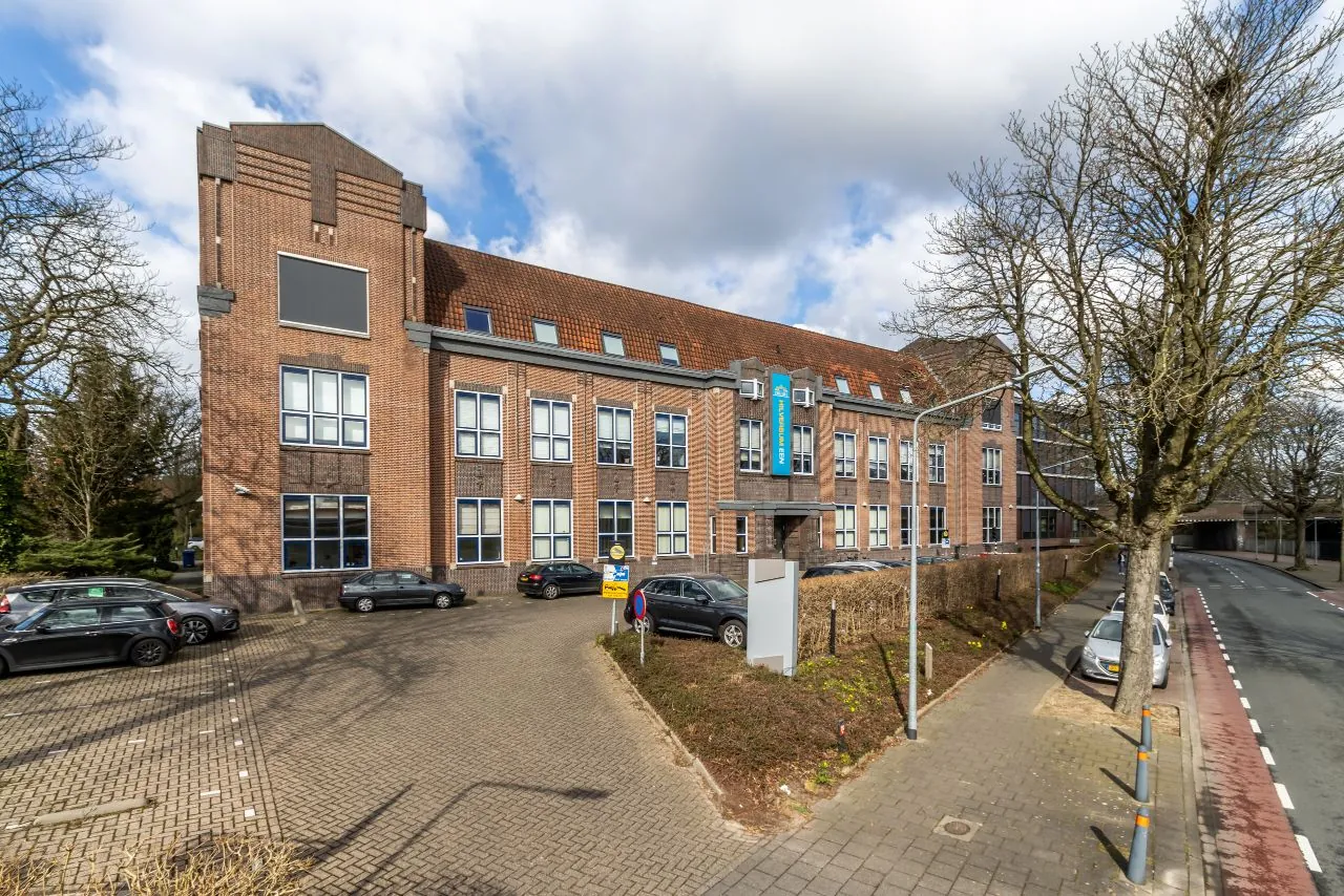 Vooraanzicht van een karakteristiek bakstenen kantoorgebouw aan de Lage Naarderweg met parkeerplaatsen en fietsenstalling.
